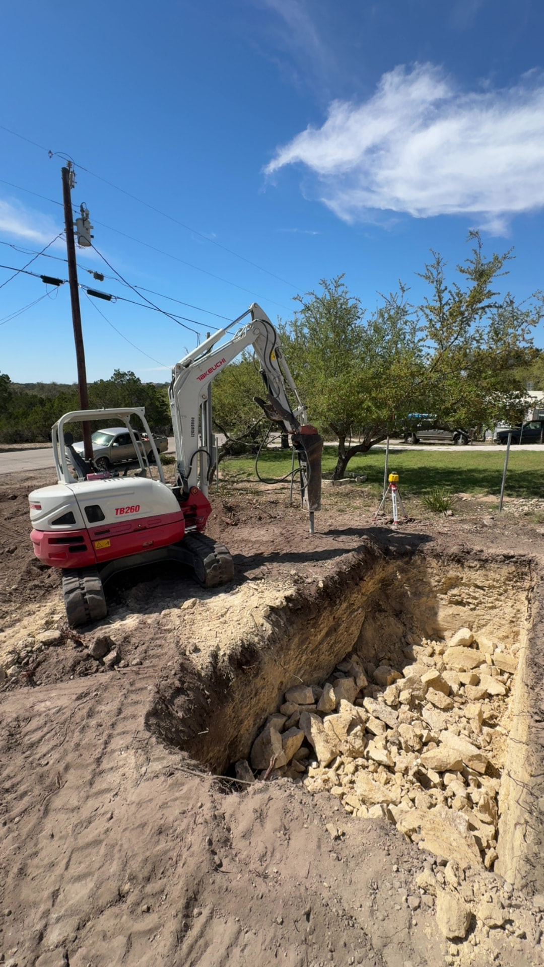 Excavator with hydraulic hammer breaking rock for a tank excavation