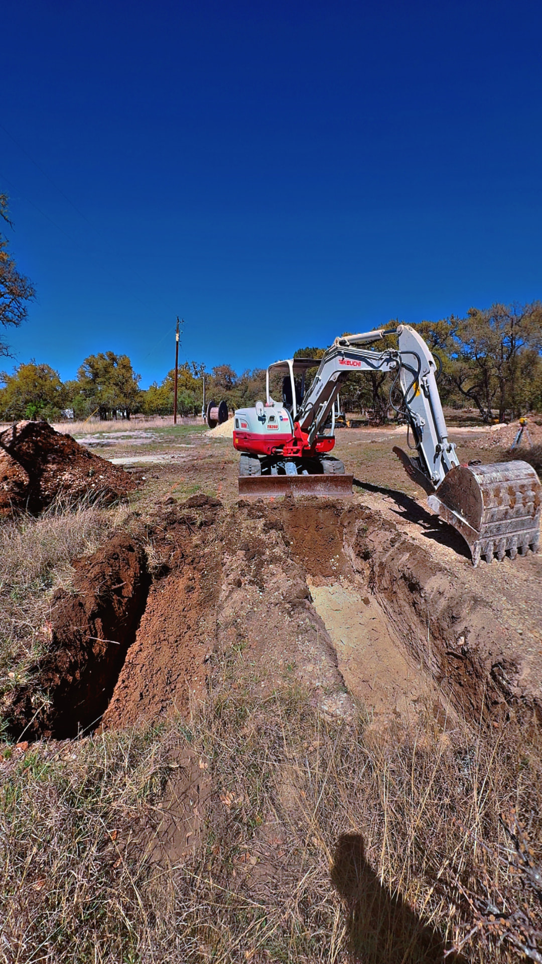 Mini excavator beside a freshly cut septic trench on a Hill Country lot